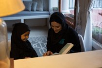 Мусульманская мать помогает дочери читать священный Коран дома — стоковое фото