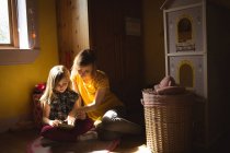 Filha com a mãe lendo um livro no quarto em casa — Fotografia de Stock