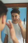 Homem aplicando creme facial na frente do espelho em casa . — Fotografia de Stock