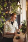 Чоловік використовує мобільний телефон, маючи каву в кафе — стокове фото