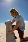 Homem aplicando cera de prancha para sandboard no deserto em um dia ensolarado — Fotografia de Stock