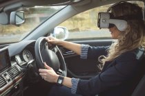 Vista lateral de la ejecutiva femenina usando auriculares de realidad virtual mientras conduce un automóvil - foto de stock