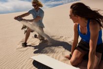 Casal verificando sandboard em duna de areia no deserto — Fotografia de Stock