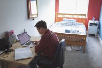 Молодий чоловік використовує ноутбук за столом в інтер'єрі спальні . — стокове фото