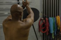 Rear view of man exercising with barbell in fitness studio. — Stock Photo