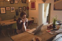 Frau trinkt Kaffee, während sie zu Hause Laptop benutzt. — Stockfoto