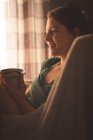 Jovem mulher tomando café em poltrona em casa . — Fotografia de Stock