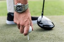 Человек регулирует мяч для гольфа на Ти в поле для гольфа — стоковое фото