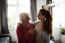 Улыбающиеся бабушка и внучка стоят с рукой в гостиной — стоковое фото
