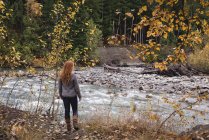 Rückansicht einer Frau, die im Herbstwald in Richtung Fluss läuft — Stockfoto