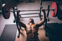 Sobrecarga de homem musculoso exercitando com barbell no estúdio de fitness — Fotografia de Stock