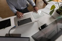 Бизнесмен, использующий стеклянный цифровой планшет во время работы на ноутбуке в офисе . — стоковое фото