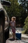 Девушка заливает воду в ведро во время мытья машины — стоковое фото