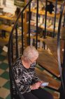 Старша жінка використовує мобільний телефон в магазині антикварних книг — стокове фото