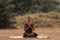 Mujer en forma sentada en postura de meditación en un campo abierto y un día soleado - foto de stock