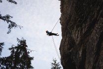 Vista de ángulo bajo del escalador escalando el acantilado rocoso - foto de stock