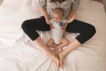 Niedliches kleines Baby zwischen Mutterbeinen zu Hause im Bett — Stockfoto