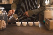 Barista pouring coffee into cups at counter in coffee shop — Stock Photo