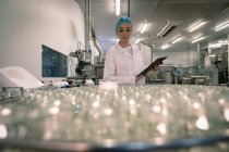 Trabalhadora monitorando os frascos de vidro na linha de produção na fábrica — Fotografia de Stock