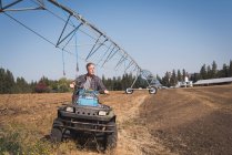 Agricultor dirigindo veículo terrestre no campo em um dia ensolarado — Fotografia de Stock