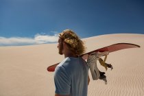 Hombre con tabla de arena caminando en el desierto en un día soleado - foto de stock