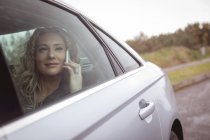 Mujer de negocios sonriente hablando por teléfono en el asiento trasero del coche - foto de stock