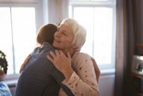 Старша жінка і дочка обнімаються у вітальні вдома — стокове фото