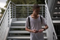 Jeune homme vérifiant l'heure sur montre-bracelet tout en utilisant un téléphone portable dans les escaliers — Photo de stock