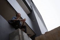 Продуманий молодий чоловік використовує мобільний телефон, сидячи на балконі — стокове фото