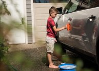 Хлопчик миє машину в гаражі в сонячний день — стокове фото