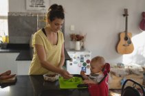 Mother feeding her baby in kitchen at home — Stock Photo