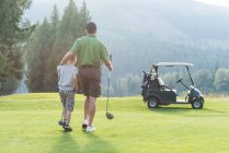 Вид ззаду батька і сина, що йде з гольф-клубом на трасі — стокове фото