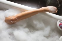 Cropped view of leg of woman taking bath with foam in bathtub at home. — Stock Photo