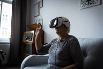 Старша жінка використовує гарнітуру віртуальної реальності у вітальні вдома — стокове фото