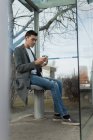 Mann benutzt Handy beim Kaffeetrinken an Bushaltestelle — Stockfoto