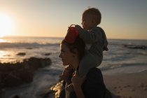 Mãe e filho se divertindo na praia durante o pôr do sol — Fotografia de Stock