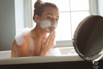 Женщина надевает маску для лица, принимая ванну в ванной комнате дома . — стоковое фото