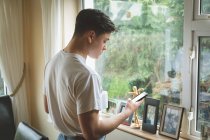 Man using mobile phone by window at home. — Stock Photo