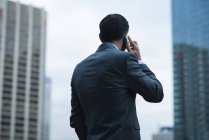 Rückansicht eines Geschäftsmannes, der mit dem Handy gegen Wolkenkratzer spricht — Stockfoto