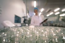 Trabalhadora monitorando os frascos de vidro na linha de produção na fábrica — Fotografia de Stock