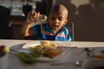Boy sprinkling salt on food at home table. — Stock Photo