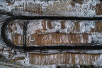 Стопка деревянных бревен, хранящихся среди заснеженной извилистой дороги зимой — стоковое фото