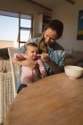 Mother feeding baby boy by table at home. — Stock Photo