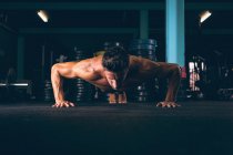 Hombre musculoso decidido haciendo push-up en el gimnasio - foto de stock