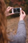 Close-up of woman taking a photo with phone in autumn forest — Stock Photo