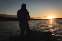 Человек рыбачит на моторной лодке в реке на закате . — стоковое фото