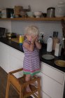 Toddler girl standing on chair in kitchen at home. — Stock Photo