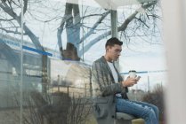 Mann benutzt Handy beim Kaffeetrinken an Bushaltestelle — Stockfoto