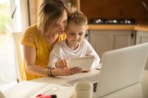 Mutter mit Sohn sitzt mit digitalem Tablet in der heimischen Küche auf Stuhl — Stockfoto