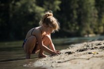 Girl playing with sand near riverbank on a sunny day — Stock Photo